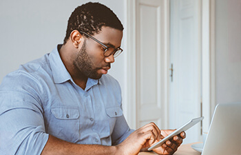 Male student working on a laptop and looking at his phone