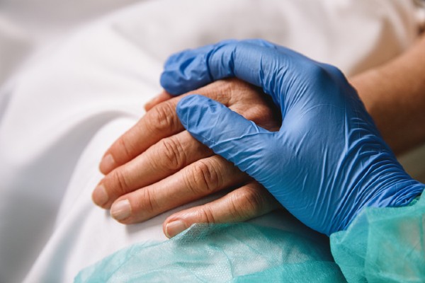 Close-up of a nurse’s hand holding a patient’s hand, showing support and care.