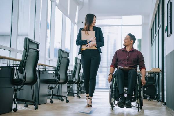 A man sits in a wheelchair and talks to a woman in an office.