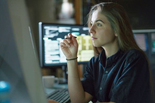 Woman working at desk surrounded by monitors with data