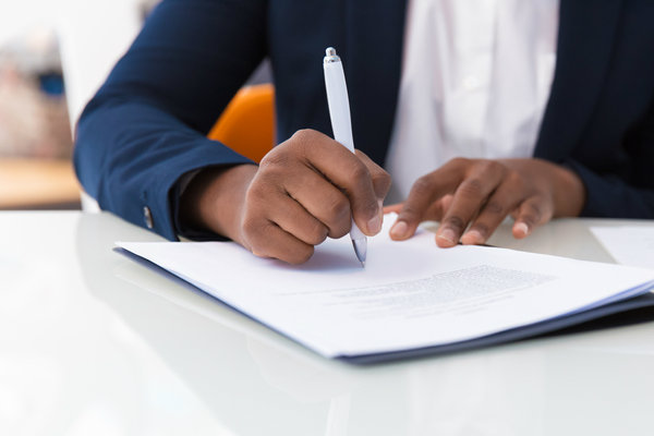 Paralegal sitting at table in office, holding pen and writing in document.
