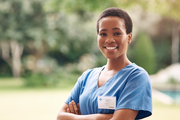 A minority nurse stands outside in her scrubs