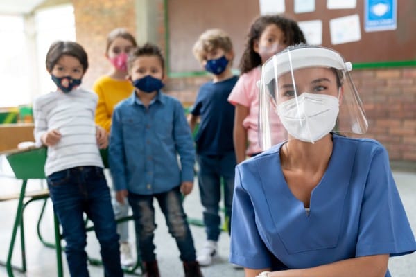 A school nurse visits a classroom safely with a mask and shield.