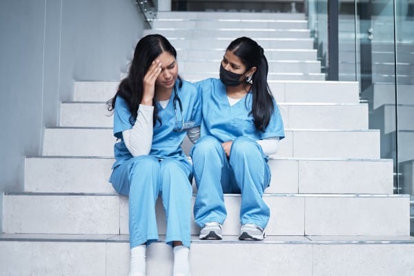 Two nurses sit on some stairs wearing scrubs
