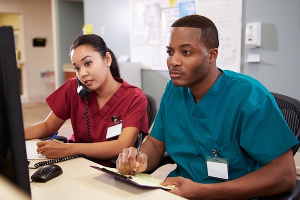 A male and a female nurse look at a compuater screen in a hospital