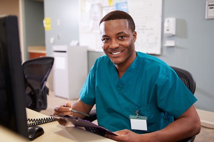 smiling male nurse in scrubs sitting at a front desk
