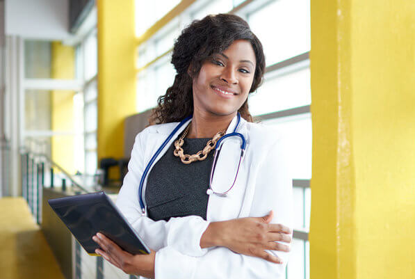 smiling African American nurse in white coat holding a tablet