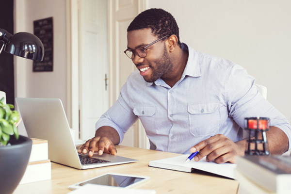 A man sits at a desk and looks at a laptop