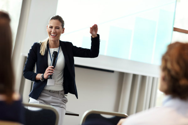 A smiling woman gives a speech before a small group of people.