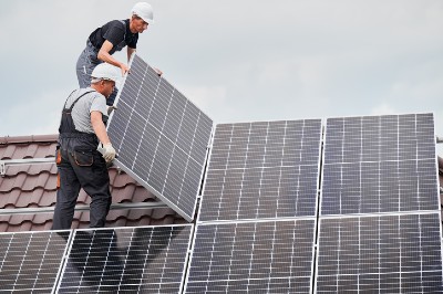 Two people install solar panels on the roof of a building