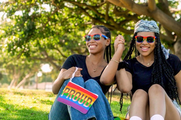 Two college students hold hands and display a rainbow pride (LGBTQ) flag accessory.