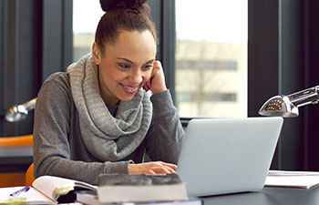 Women with grey scarf and grey shirt sitting in a modern office looking at laptop and smiling