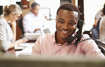 African-American man sitting in front of a computer talking on a landline telephone