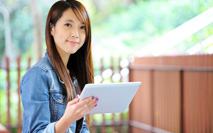 Girl with long dark hair sitting outside with tablet
