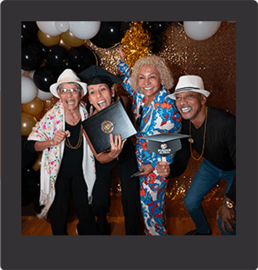 Two smiling Purdue Global graduates dancing in front of a gold background, surrounded by black and gold ballooons and bubbles