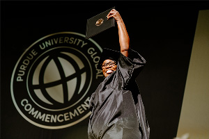 Purdue Global graduate walking across the stage at graduation and raising a diploma
