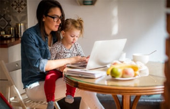Female student working on a laptop with a child on her lap